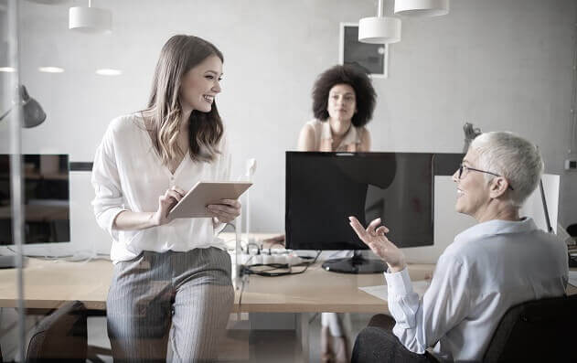 Mujeres profesionales conversan en una oficina moderna mientras una de ellas toma notas con una tablet