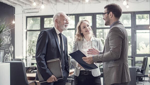 Tres profesionales de negocios conversan y revisan documentos en una oficina moderna con luz natural